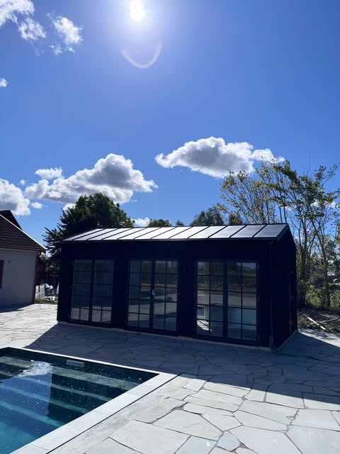 Färdigt poolhus med svart fasad, plåttak och spröjsade glaspartier