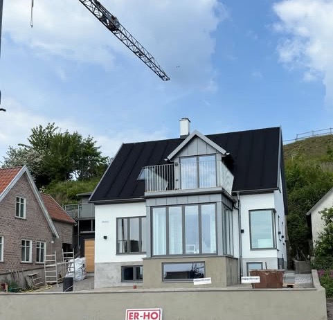 Putsad villa med ljus fasad, plåttak och burspråk